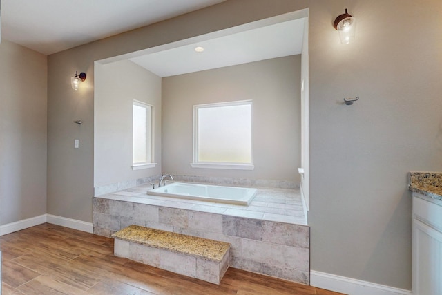 bathroom featuring tiled bath, wood-type flooring, and vanity