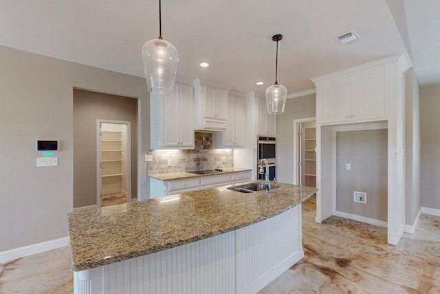 kitchen with hanging light fixtures, white cabinetry, sink, and an island with sink