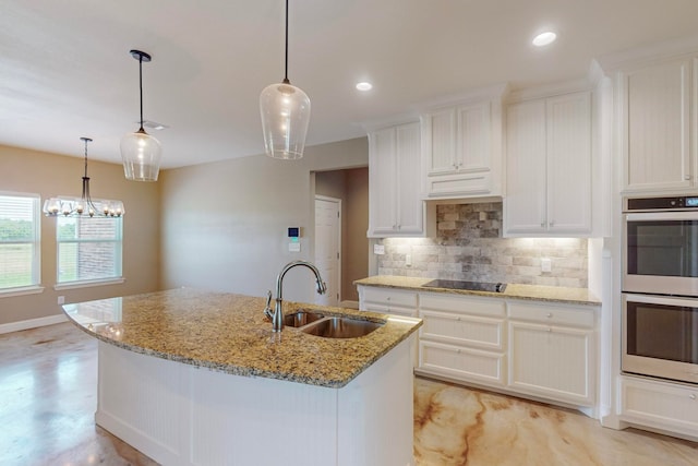 kitchen featuring an island with sink, light stone counters, white cabinets, stainless steel double oven, and sink