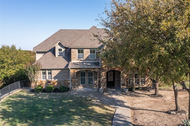 view of front facade featuring fence, stone siding, roof with shingles, and a front yard