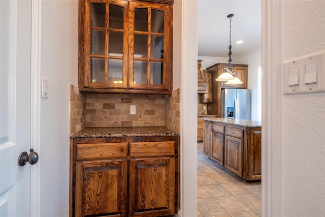 bar featuring tasteful backsplash, crown molding, hanging light fixtures, light tile patterned floors, and stainless steel refrigerator with ice dispenser