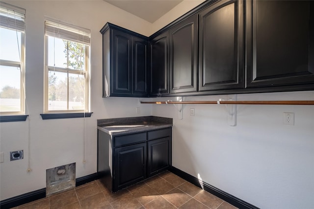 laundry area featuring electric dryer hookup, baseboards, dark tile patterned floors, and cabinet space