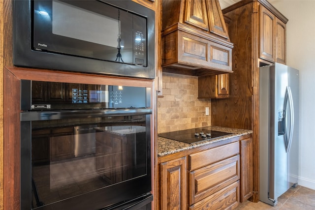 kitchen with dark stone countertops, black appliances, brown cabinets, light tile patterned floors, and backsplash
