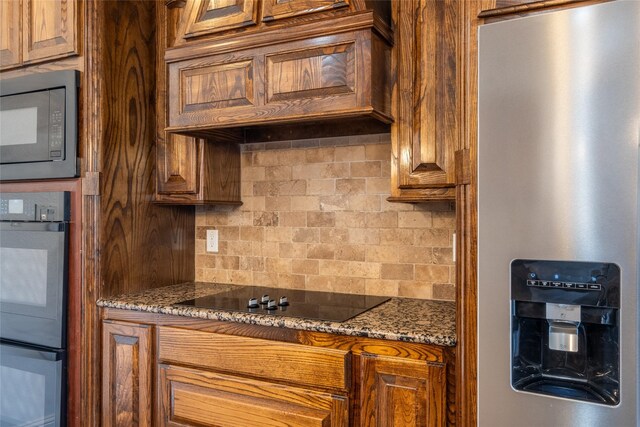 kitchen with brown cabinetry, black appliances, stone countertops, custom range hood, and backsplash