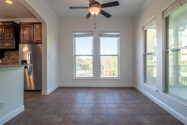 unfurnished dining area with ceiling fan, arched walkways, crown molding, and baseboards