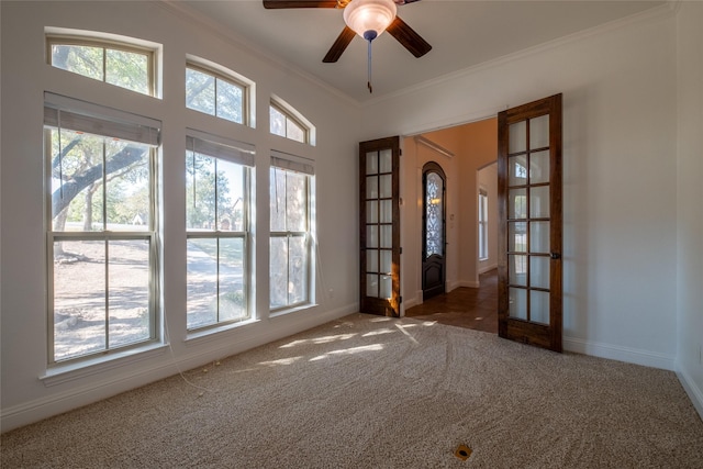 carpeted spare room with plenty of natural light, crown molding, a ceiling fan, and french doors