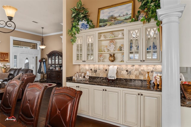 bar featuring tasteful backsplash, dark stone countertops, crown molding, hanging light fixtures, and decorative columns