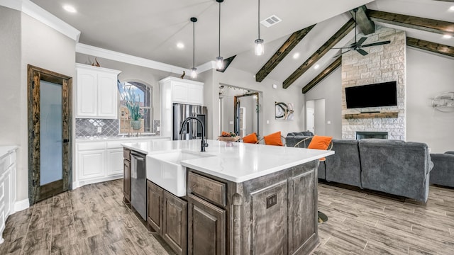 kitchen with stainless steel appliances, an island with sink, white cabinets, and vaulted ceiling with beams