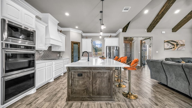 kitchen featuring an island with sink, hanging light fixtures, white cabinetry, hardwood / wood-style flooring, and stainless steel appliances