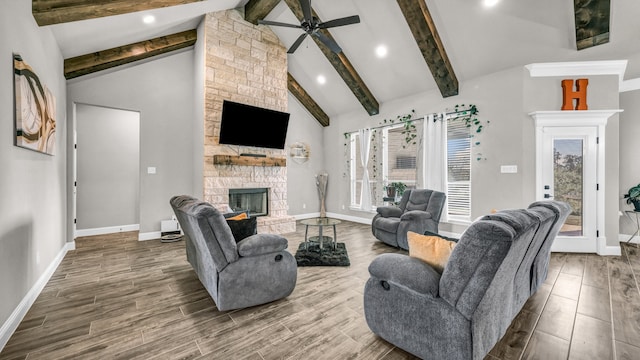 living room with ceiling fan, beam ceiling, a stone fireplace, high vaulted ceiling, and hardwood / wood-style flooring