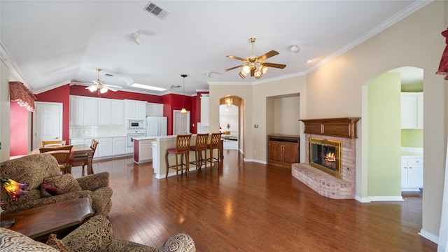 living room with ceiling fan, ornamental molding, dark wood-type flooring, a fireplace, and vaulted ceiling