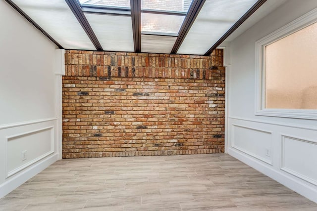 spare room featuring a healthy amount of sunlight, brick wall, and light hardwood / wood-style flooring