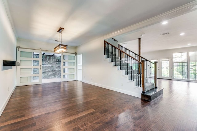 unfurnished living room featuring ornamental molding, a barn door, and dark wood-type flooring