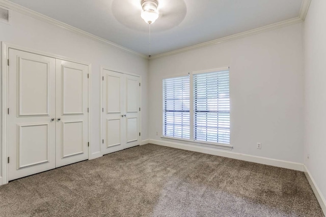 unfurnished bedroom with ceiling fan, multiple closets, light carpet, and ornamental molding