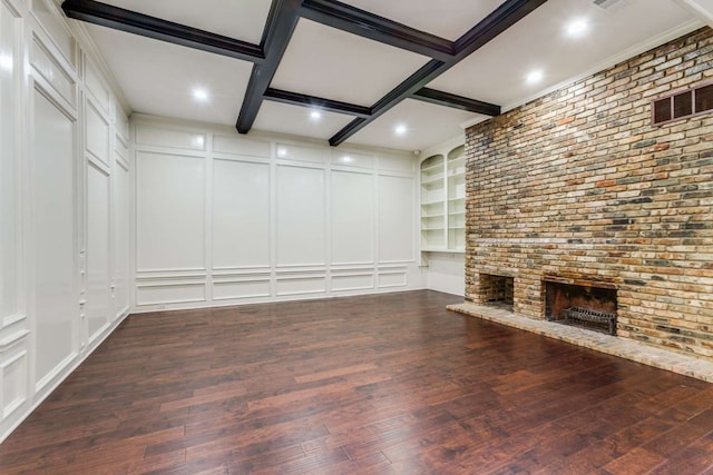 unfurnished living room with built in features, beam ceiling, a brick fireplace, coffered ceiling, and dark hardwood / wood-style flooring