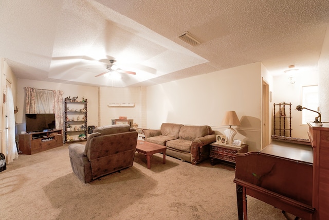 living room featuring light carpet, ceiling fan, a tray ceiling, and a textured ceiling