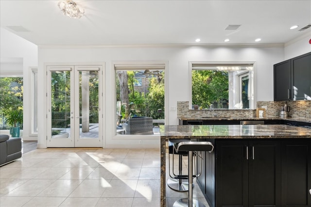 interior space with ornamental molding, decorative backsplash, dark stone counters, and light tile patterned floors