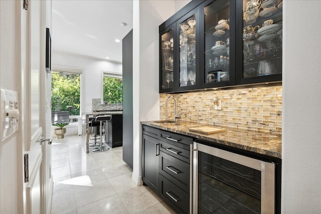 bar with stone counters, light tile patterned flooring, sink, beverage cooler, and decorative backsplash