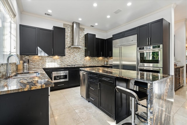 kitchen featuring appliances with stainless steel finishes, dark stone countertops, sink, wall chimney exhaust hood, and a center island