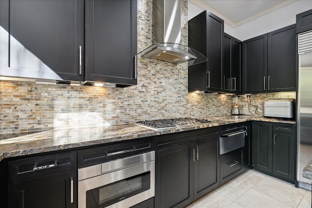 kitchen with wall chimney range hood, tasteful backsplash, stone countertops, and appliances with stainless steel finishes