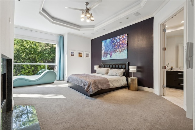 carpeted bedroom featuring crown molding, a raised ceiling, ensuite bathroom, and ceiling fan