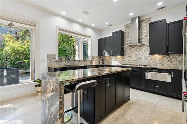 kitchen with wall chimney range hood, decorative backsplash, dark stone countertops, and a kitchen island