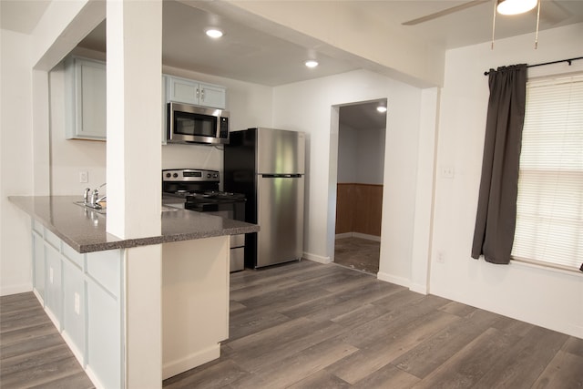 kitchen with kitchen peninsula, appliances with stainless steel finishes, dark stone counters, white cabinets, and dark hardwood / wood-style floors