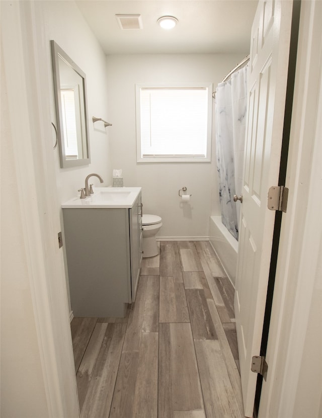 full bathroom with hardwood / wood-style floors, vanity, shower / tub combo, and toilet