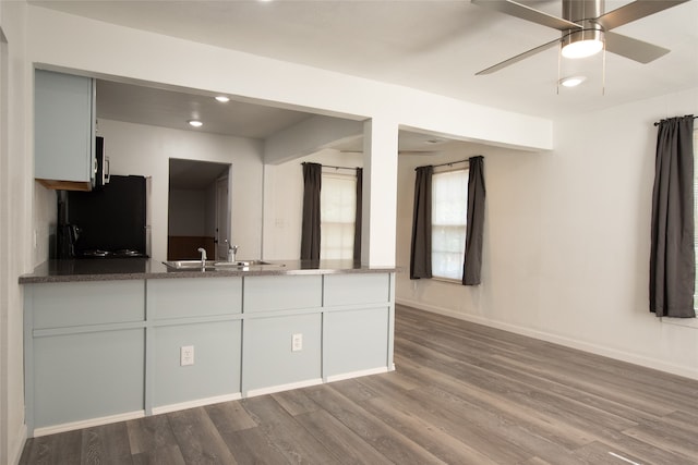 kitchen with white cabinetry, sink, ceiling fan, black fridge, and hardwood / wood-style flooring