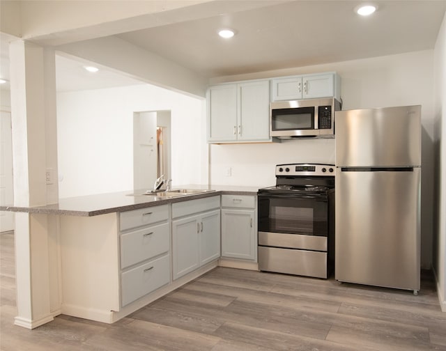 kitchen with white cabinets, light hardwood / wood-style floors, kitchen peninsula, and appliances with stainless steel finishes