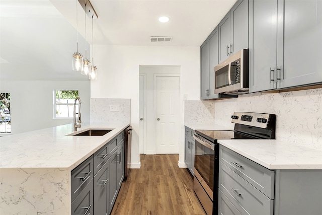 kitchen featuring gray cabinetry, wood-type flooring, appliances with stainless steel finishes, sink, and decorative light fixtures