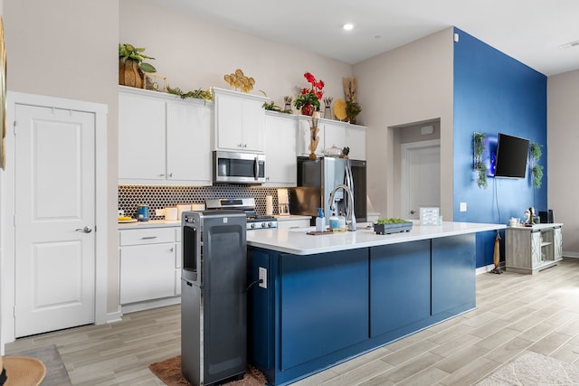 kitchen featuring white cabinetry, light hardwood / wood-style floors, appliances with stainless steel finishes, and a kitchen island with sink