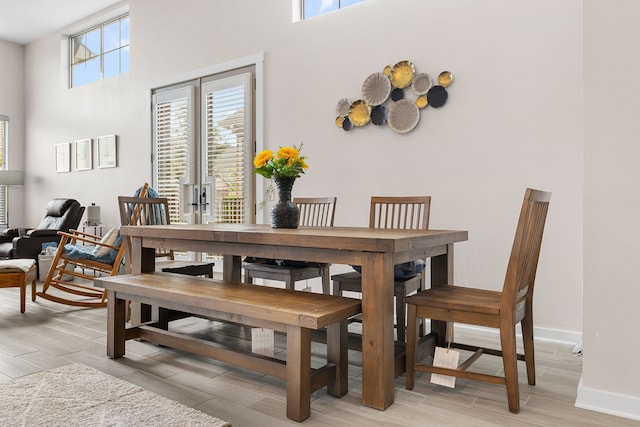 dining space featuring a high ceiling, a healthy amount of sunlight, and light hardwood / wood-style floors