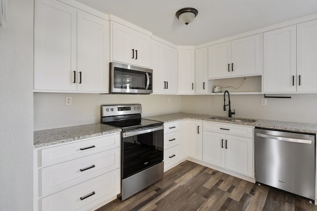 kitchen with appliances with stainless steel finishes, sink, white cabinets, dark wood-type flooring, and light stone counters