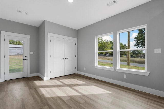 unfurnished bedroom with a closet, light hardwood / wood-style floors, and multiple windows