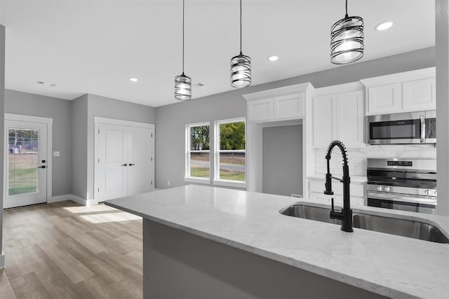 kitchen with light stone counters, pendant lighting, stainless steel appliances, and white cabinetry