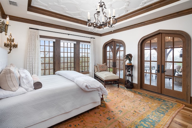 bedroom featuring an inviting chandelier, access to exterior, hardwood / wood-style floors, crown molding, and french doors