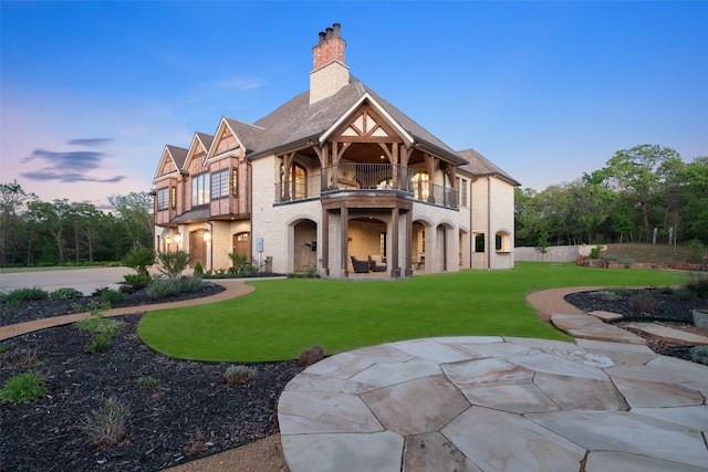 back house at dusk with a balcony, a yard, and a patio area