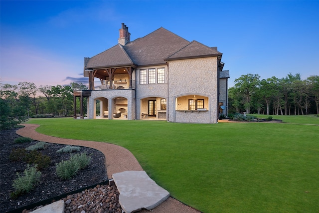 back house at dusk featuring a balcony and a lawn