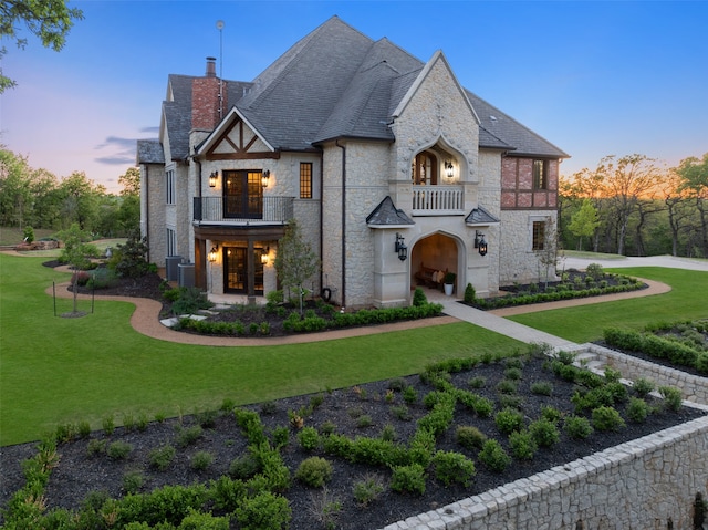 view of front facade featuring central AC unit, a balcony, and a lawn