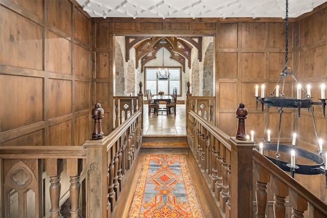 corridor with wood walls, hardwood / wood-style floors, and a notable chandelier