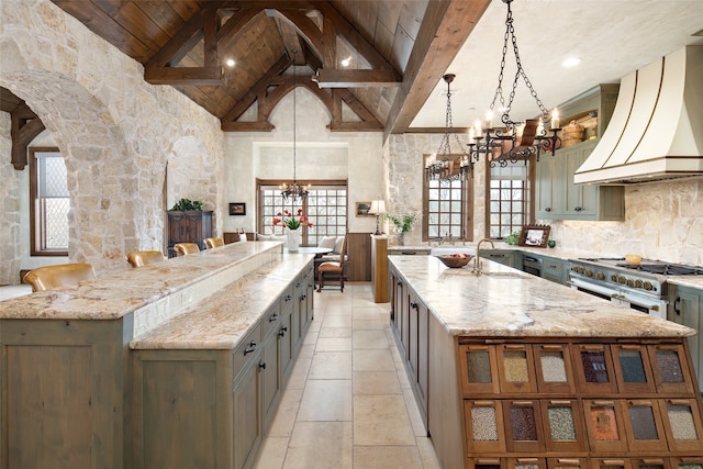 kitchen featuring custom exhaust hood, hanging light fixtures, high end range, a large island with sink, and an inviting chandelier