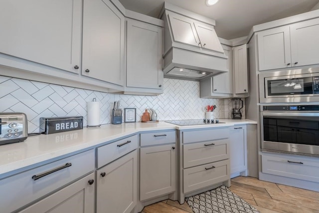 kitchen with appliances with stainless steel finishes, decorative backsplash, white cabinets, and custom exhaust hood