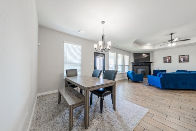 dining space featuring ceiling fan with notable chandelier, a raised ceiling, and light hardwood / wood-style floors