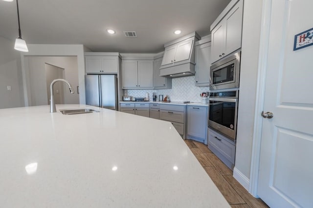 kitchen featuring light wood-type flooring, decorative light fixtures, sink, custom exhaust hood, and appliances with stainless steel finishes