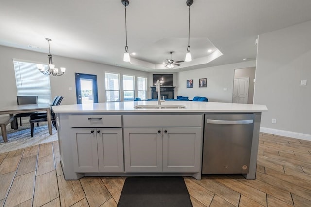 kitchen featuring light wood-type flooring, sink, ceiling fan with notable chandelier, a tray ceiling, and dishwasher