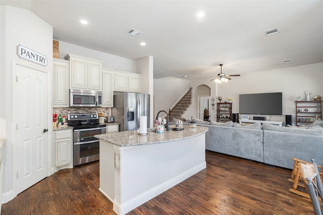 kitchen with decorative backsplash, dark wood-type flooring, light stone counters, stainless steel appliances, and an island with sink