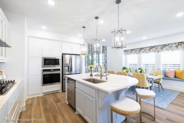 kitchen featuring light hardwood / wood-style floors, sink, stainless steel appliances, an island with sink, and white cabinetry