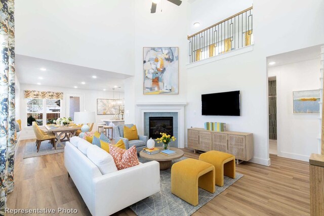 living room with ceiling fan, a fireplace, a towering ceiling, and light hardwood / wood-style floors