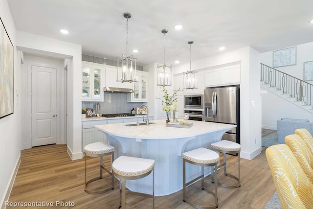 kitchen with a kitchen island with sink, stainless steel appliances, sink, white cabinetry, and light hardwood / wood-style flooring